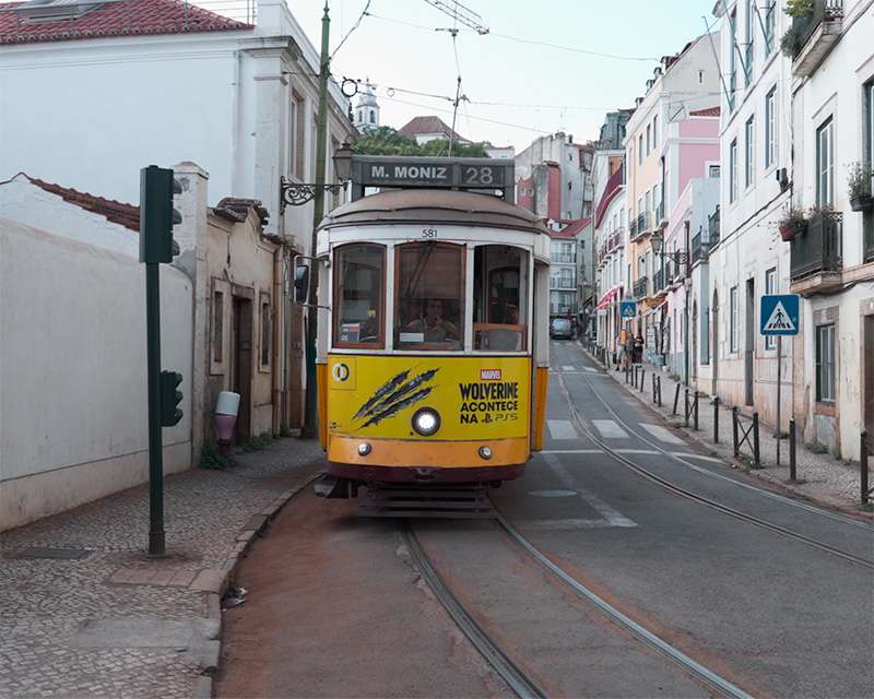 Gelbe Straßenbahn 28 auf den Schienen zwischen weißen Hausfronten in der Alfama