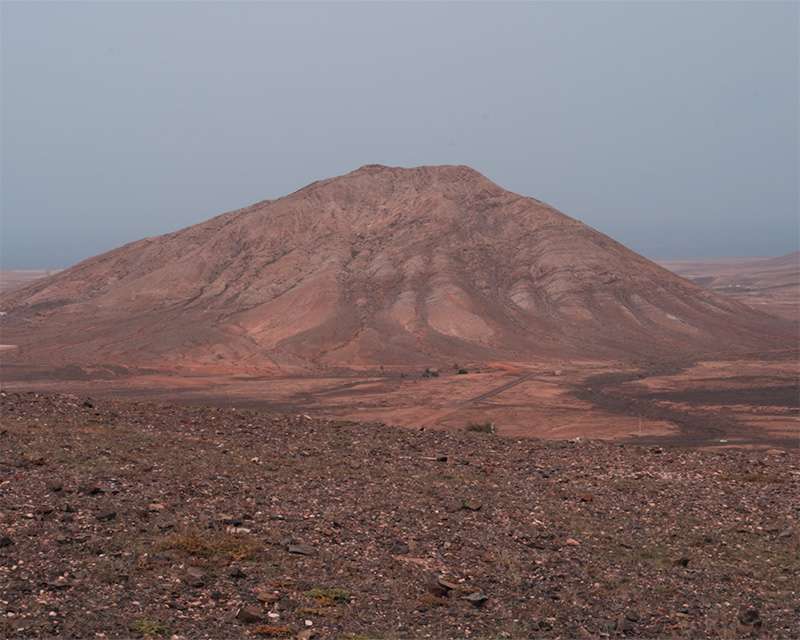 Bare volcanic cone rising out of flat ground in the haze, northern Fuerteventura