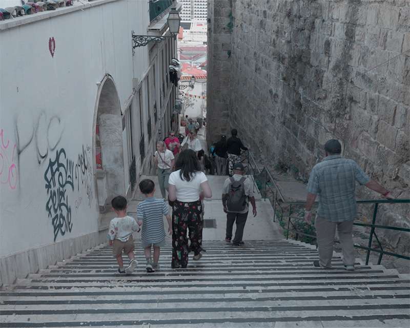 Besucher auf der Steintreppe zwischen Burgmauer und bemalter Wand über Lissabon