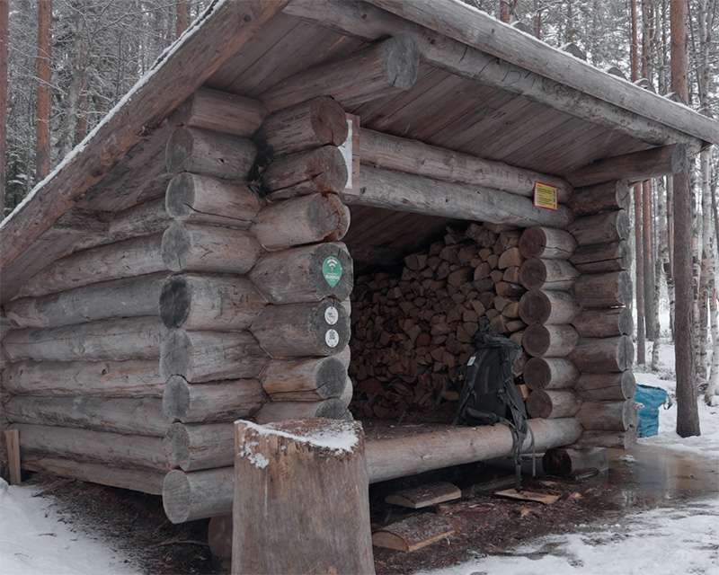 Log shelter with stacked firewood beside the Pilpasuo nature trail in winter