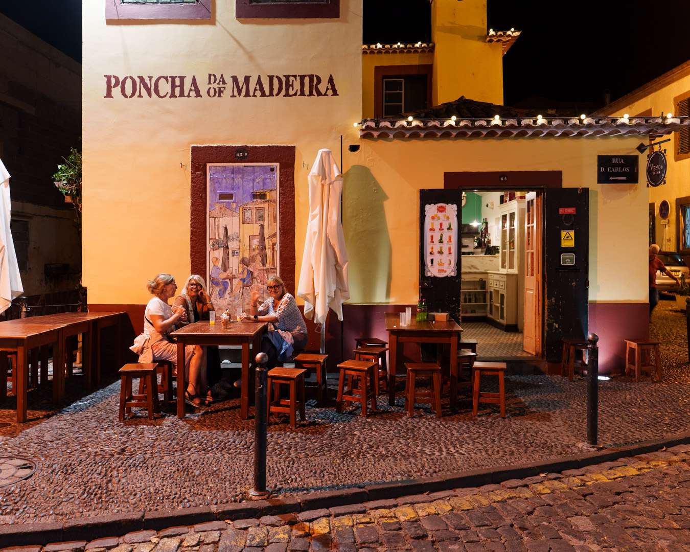 Poncha bar with wooden tables and guests on a corner of Funchal old town in the evening