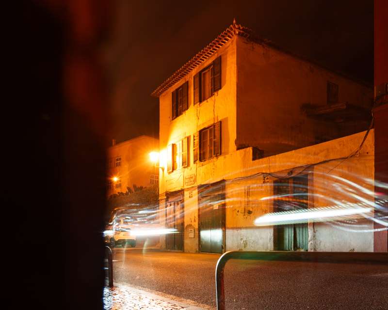 Light trail of a vehicle in front of an ochre old town house in Funchal at night