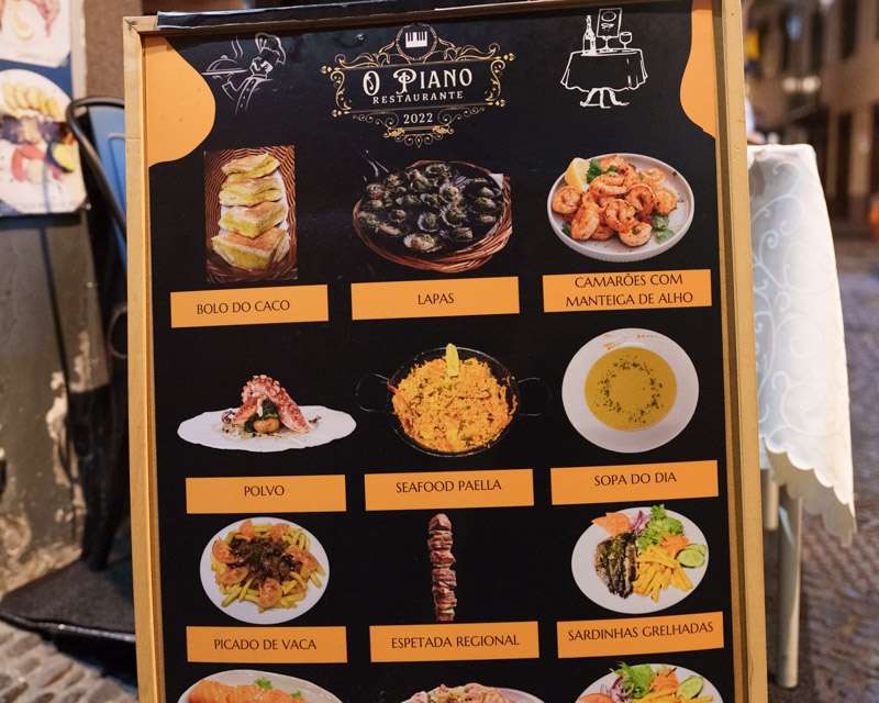 Board with photographs of dishes outside a restaurant in Funchal old town, no prices shown