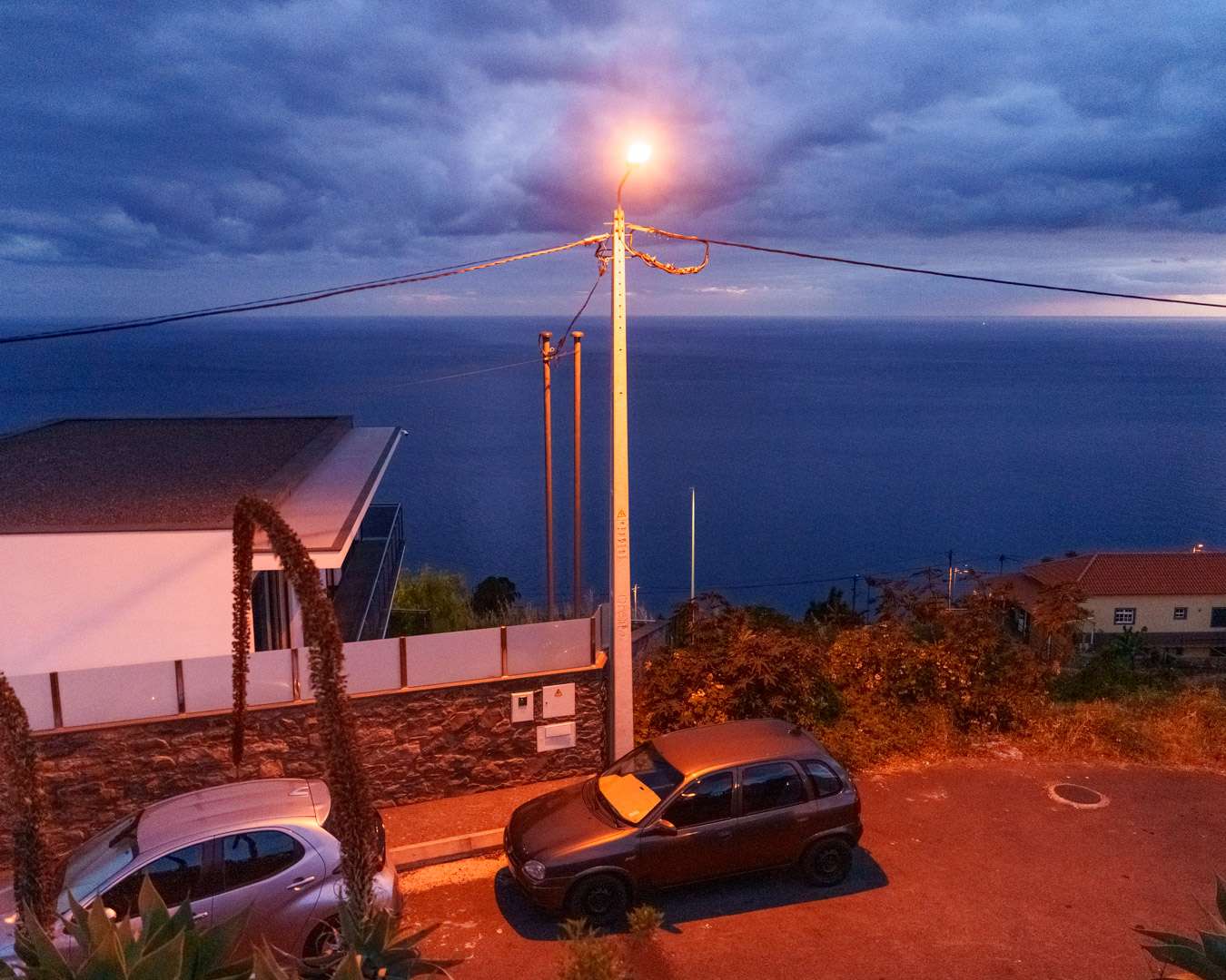 Roadside viewpoint above Funchal at blue hour with a street lamp and the sea beyond