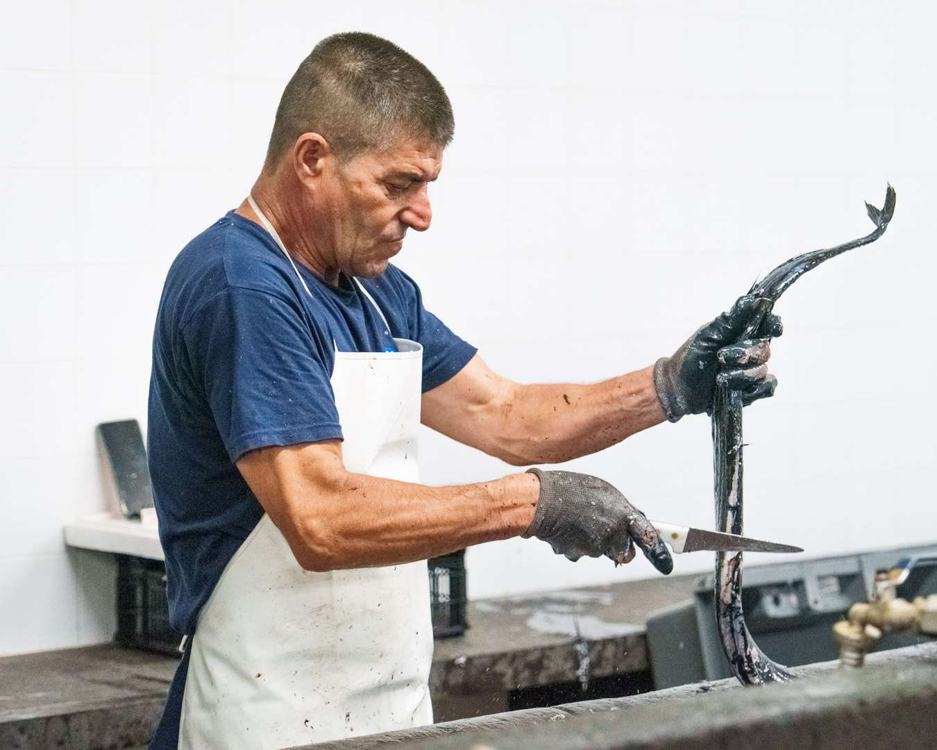 Fishmonger filleting a black scabbard fish on the stone counter of Funchal's fish hall