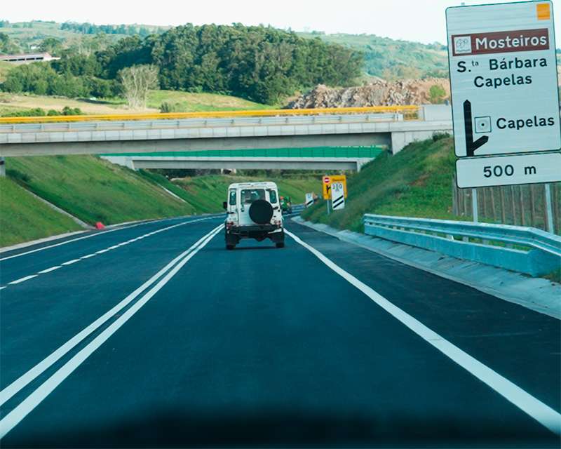 Motorway sign for Mosteiros and Capelas with a Land Rover ahead, São Miguel